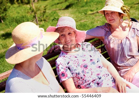 Portrait of three senior females sitting on bench at summer and chatting