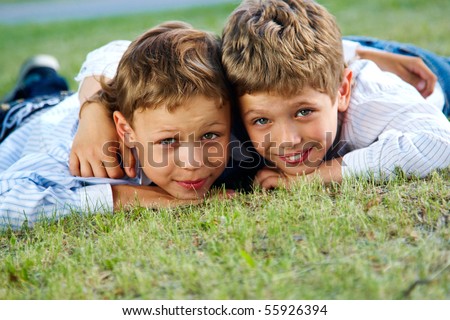 Portrait of happy boys lying on green grass and smiling at camera