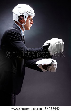 Portrait of young businessman in suit and hockey helmet and gloves fighting
