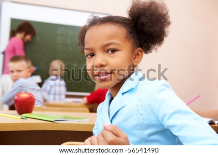 Portrait of happy and smart girl smiling at camera during lesson in classroom