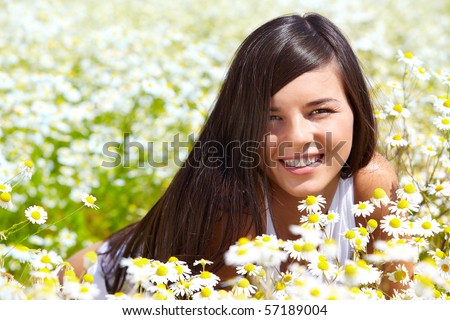 Image of happy female peeking out of chamomile glade and smiling at camera
