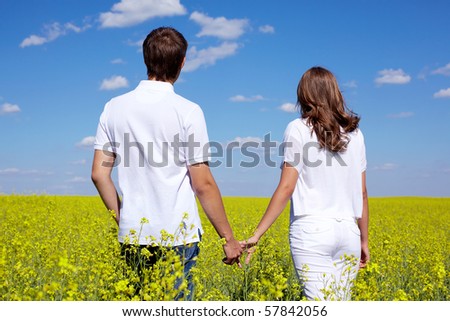 Back view of amorous couple walking in yellow meadow at summer