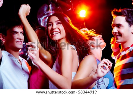Photo of energetic girl dancing in the night club with her friends on background Photo of energetic girl dancing in the night club with her friends on background