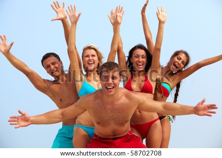 Portrait of joyful guy and happy girls in bikini on background looking at camera on summer vacation