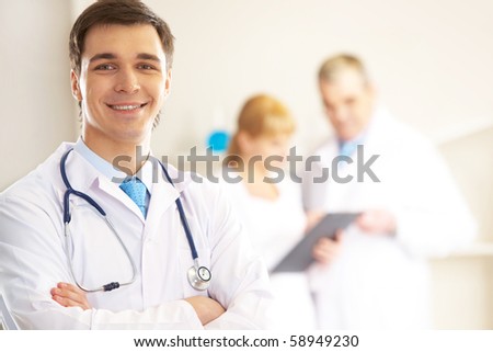 Portrait of cheerful doctor looking at camera and smiling with working clinicians behind