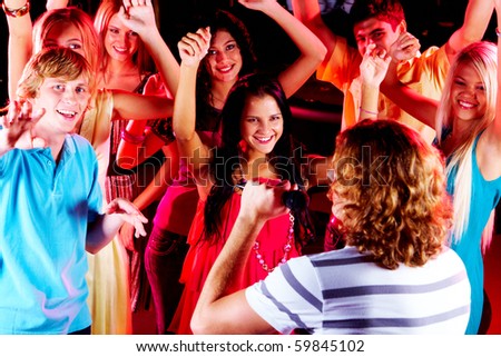 Photo of happy teenage friends looking at guy singing in mic at party