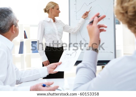 Photo of successful manager standing by whiteboard while her colleagues listening to her