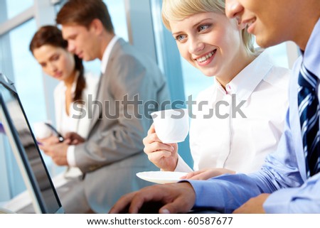 Portrait of young female with cup of coffee looking at laptop monitor in office and interacting with partner