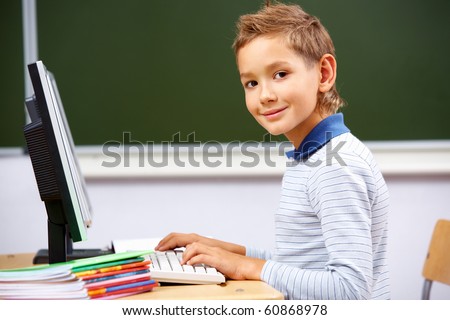 Portrait of cute lad typing on computer board and looking at camera in classroom