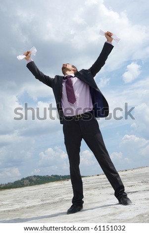 Photo of crying businessman standing and raising his arms with papers outdoors