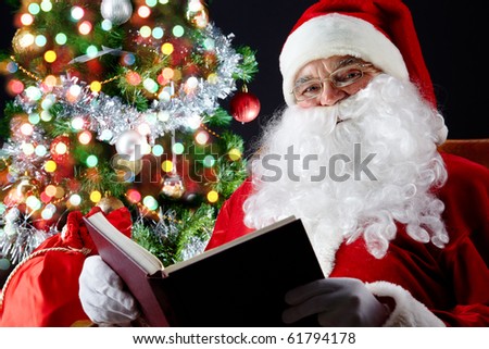 Santa sitting at the Christmas tree and reading a book