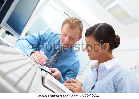 Businessman sitting at table and writing, young businesswoman sitting and looking at him
