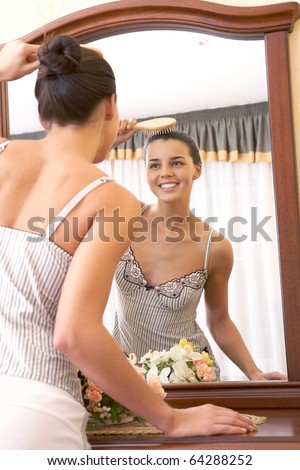 Image of pretty female looking in mirror while brushing hair