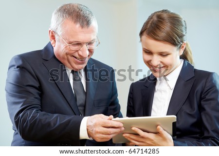 Boss and secretary looking at modern gadget with smiles during discussion