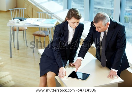 Boss pointing at tablet screen during explanation of something to secretary