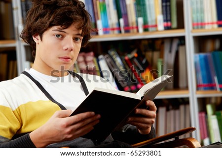 Portrait of clever student with open book reading in college library