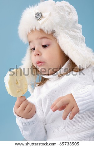 Little girl in white furry hat looking at ice-cream in her hands