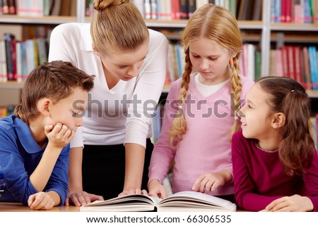 Portrait of pupils and teacher reading and discussing interesting book in library