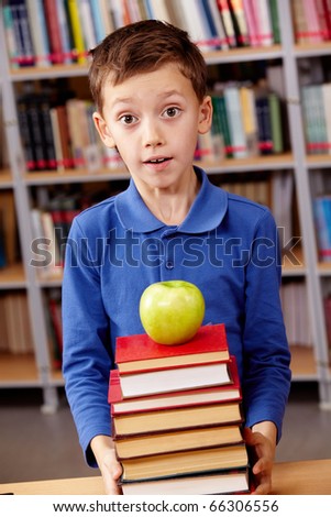 Portrait of amazed lad with green apple on top of book heap near by