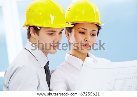 Portrait of two architects in helmets looking document at meeting