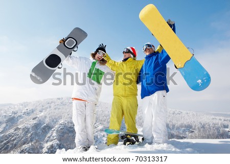 Portrait of happy three sportsmen raising their snowboards