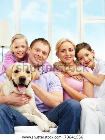 A young family of four with a dog sitting on sofa, looking at camera and smiling