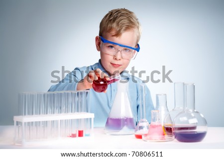 A little boy pouring liquid into a flask and looking at camera