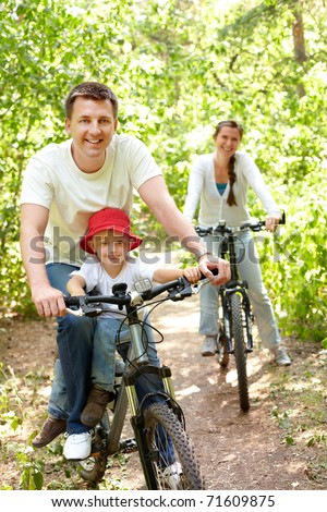Portrait of happy man with son riding a bicycle in park on background of pretty woman