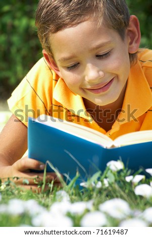 Portrait of cute schoolboy reading interesting book in natural environment
