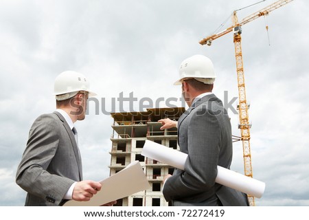 Photo of young engineer showing something to his partner at building site