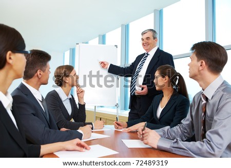 Smart and confident boss pointing at whiteboard and looking at managers during presentation