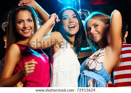 Group of fashionable girls dancing energetically in night club