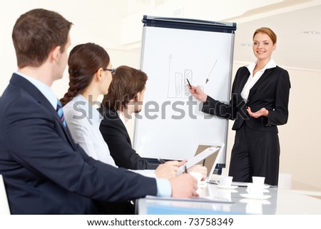 Smart and confident employee pointing at whiteboard while presenting her ideas to business partners