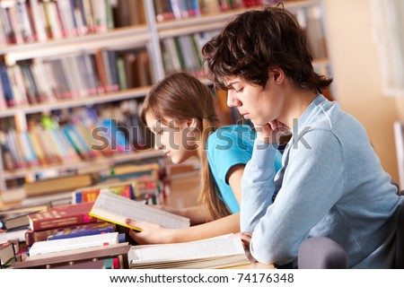 Portrait of serious guy reading book with his classmate on background