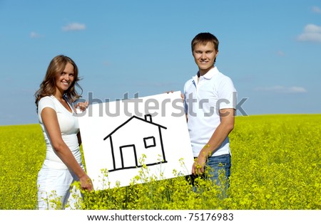 Portrait of happy young couple showing house drawn on paper in meadow