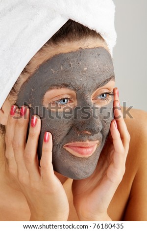 Beautiful woman with purifying facial mask keeping her palms by her face