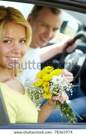 Happy woman with bunch of flowers looking at camera in the car