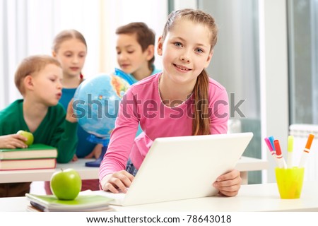 Portrait of smart schoolgirl sitting in classroom with her classmates on background