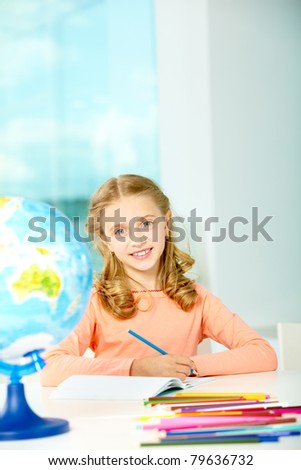 Portrait of smart schoolgirl with blue pencil looking at camera in classroom