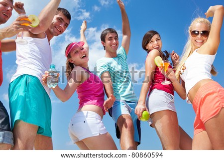 Portrait of happy young friends with cocktails dancing at beach party