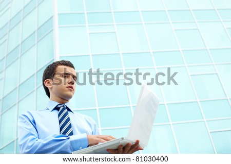Businessman standing by office building and working with computer