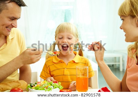 Portrait of happy parents feeding their daughter with salad in the kitchen