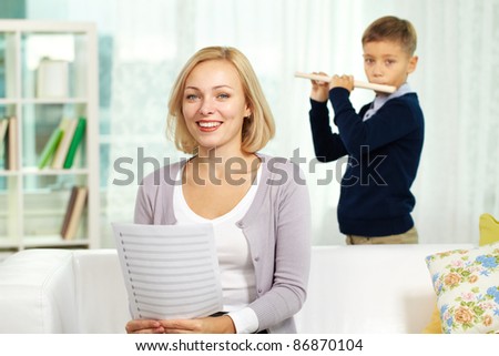 Portrait of happy tutor with notes looking at camera on background of pupil playing the flute