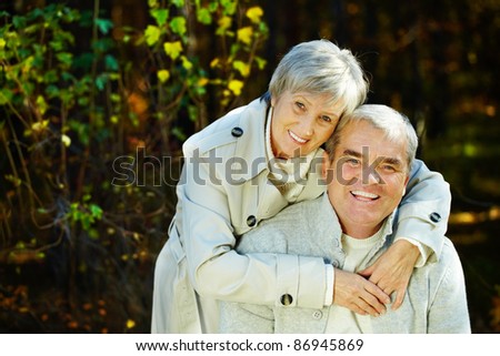 Photo of amorous aged man and woman looking at camera in autumnal park