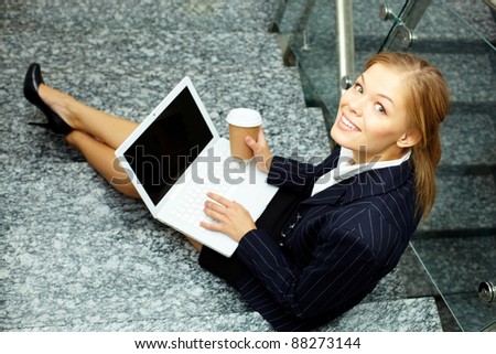 Happy businesswoman with laptop and coffee looking at camera on staircase