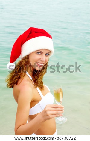 Portrait of smiling female in Santa cap holding champagne flute and looking at camera on the beach