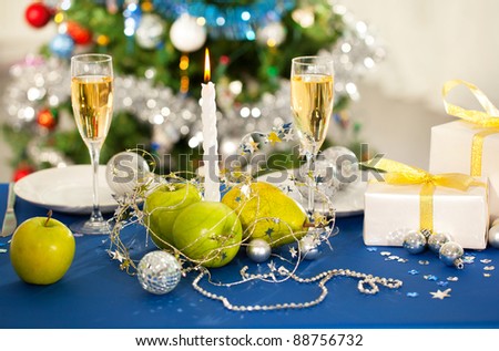 Image of holiday table with flutes of champagne, fruits, gifts, candle and plates on it