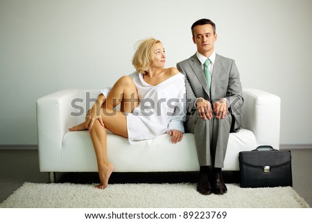 Photo of serious man sitting on sofa with seductive woman looking at him