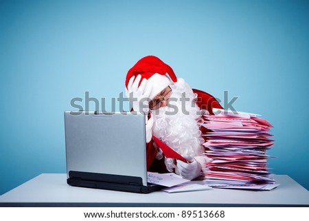 Portrait of Santa Claus touching head while looking at heap of letters in front of laptop