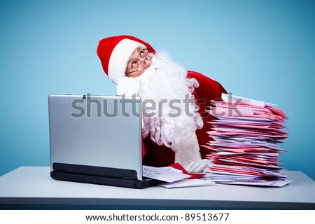 Portrait of inspired Santa Claus in front of laptop and heap of letters